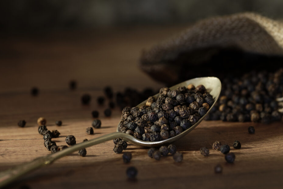 Close-up of Indian black peppercorns in a spoon on a rustic wooden table, showcasing their rich texture and aroma