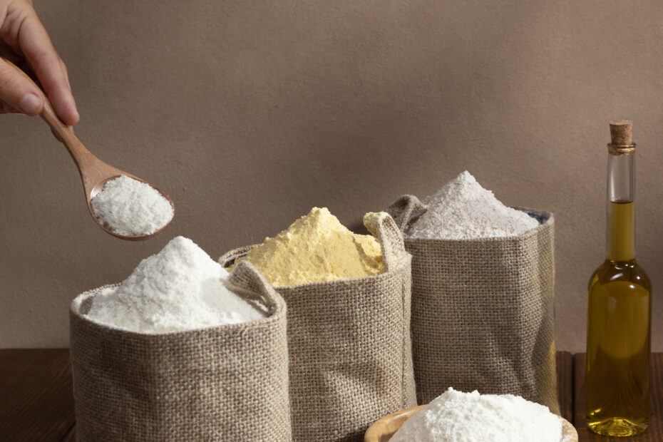 Variety of flours in jute bags with grains and oil on a rustic table, showing different flour options for chapatis — from whole wheat to multigrain and millet flours, each suited to different health goals and seasons.