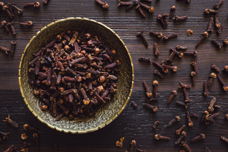Close-up of dried cloves (Laung) in a brass bowl on wooden background, a traditional Indian spice used in curries, chai, and Ayurvedic remedies.