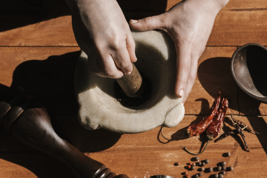 Hands grinding spices in a stone mortar and pestle on a wooden surface