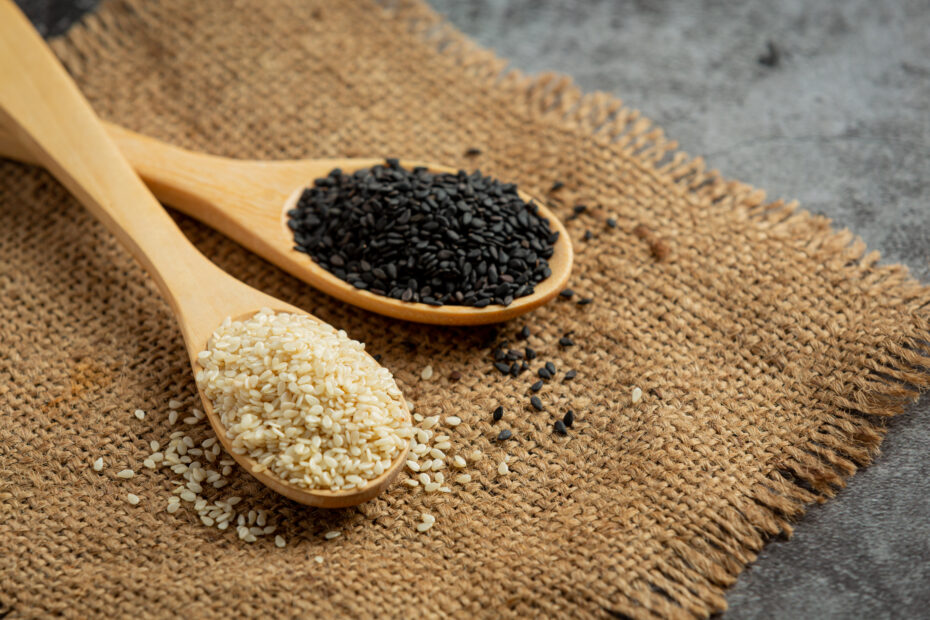 Close-up of white and black sesame seeds in wooden spoons on a jute mat, showing seed varieties used for cold-pressed sesame oil – Aara Living