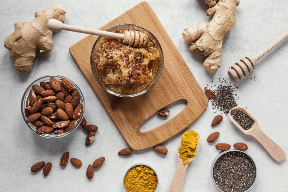 Flatlay of immunity-boosting kitchen staples including ginger, honey, turmeric, almonds, and chia seeds on a wooden board.