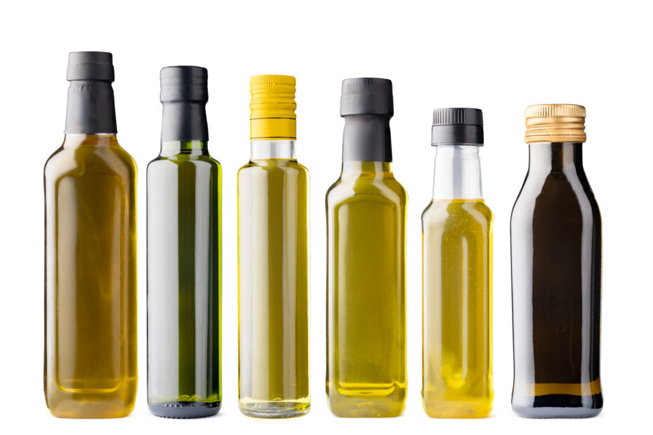 Different cooking oils in glass bottles arranged in a row, representing the practice of rotating oils like mustard, groundnut, sesame, and coconut in Indian kitchens.