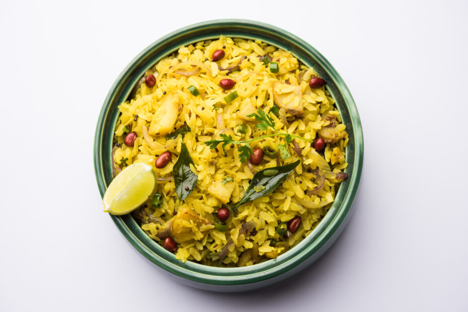 Freshly cooked poha served in a dark bowl, garnished with coriander and lemon, on a rustic green background.